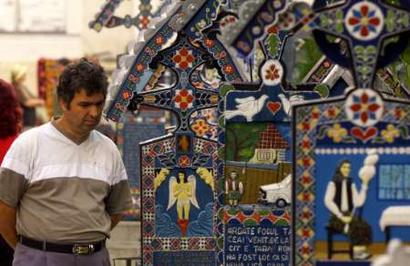 A tourist reads the epitaph writen on a painted cross in the Merry Cemetery of Sapanta (700km northwest of Bucharest) in this July 3, 2004 file picture. Bursting with colour, life and history, hundreds of brilliantly decorated wooden crosses have marked the graves of villagers since an imaginative local wood carver started this unique tradition in the 1930s.   REUTERS/Bogdan Cristel/FEATURE/ROMANIA-CEMETERY