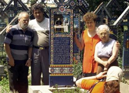 Tourists take a group picture around a painted cross in the Merry Cemetery of Sapanta (700km northwest of Bucharest) in this July 3, 2004 file picture. Bursting with colour, life and history, hundreds of brilliantly decorated wooden crosses have marked the graves of villagers since an imaginative local wood carver started this unique tradition in the 1930s.     REUTERS/Bogdan Cristel/FEATURE/ROMANIA-CEMETERY